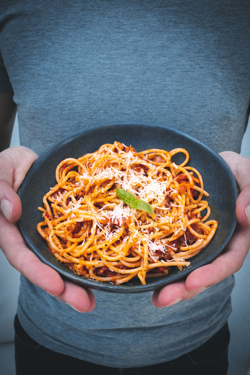 Zwei Hände halten einen Teller mit Spaghetti, Bolognese und Parmesan