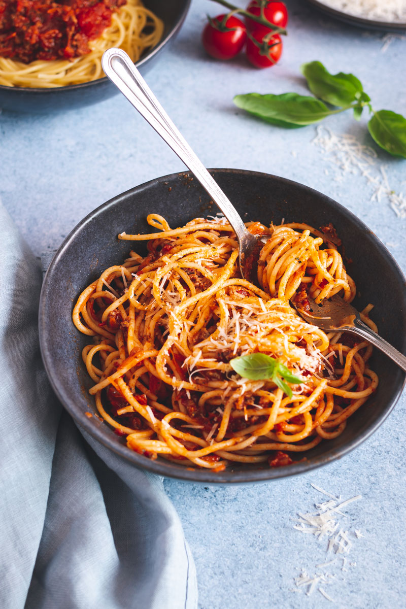 Spaghetti mit Bolognese in einem dunklen Teller mit Besteck