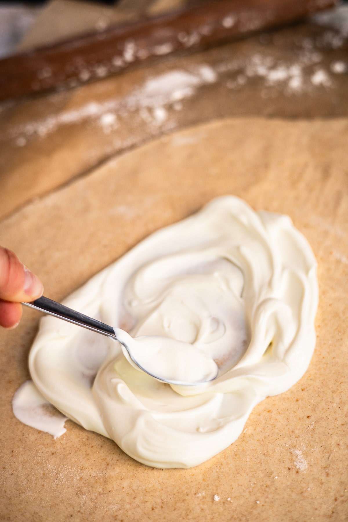 Schmand wird auf Flammkuchenteig gestrichen